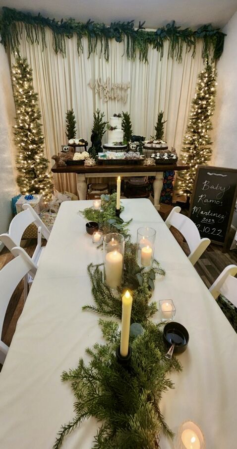 a long table with candles and greenery on it in front of a christmas tree