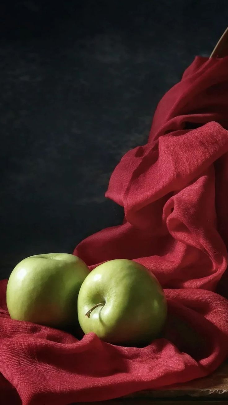 two green apples sitting on top of a red cloth