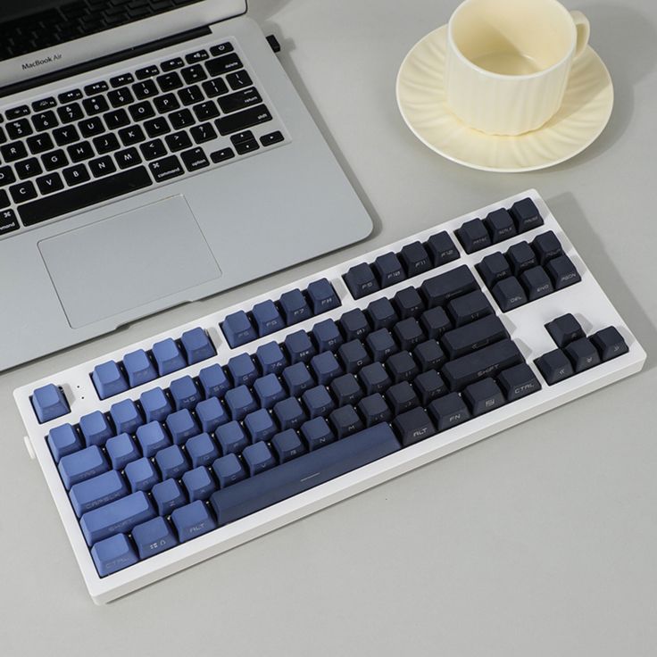 a computer keyboard sitting on top of a desk next to a cup and saucer