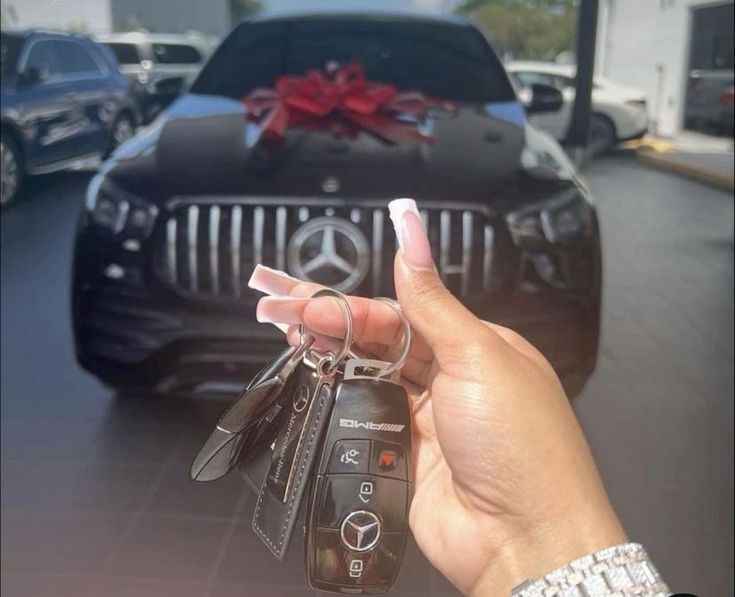 a hand holding keys in front of a mercedes car with a red bow on it