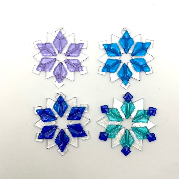 three snowflakes are shown on a white surface, one is blue and the other is purple