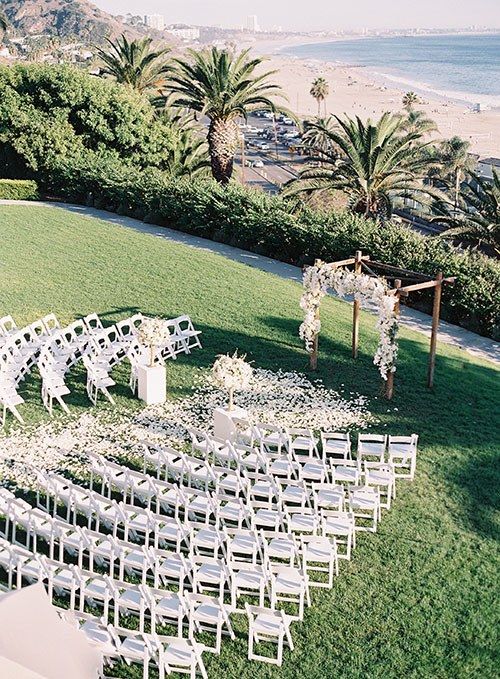 an outdoor ceremony set up with white chairs and floral arrangements on the lawn overlooking the ocean