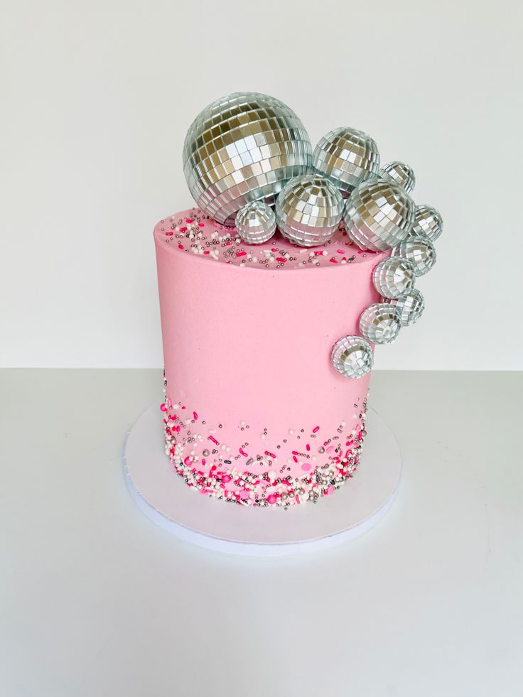 there is a pink cake with silver balls on top and confetti sprinkles all over it