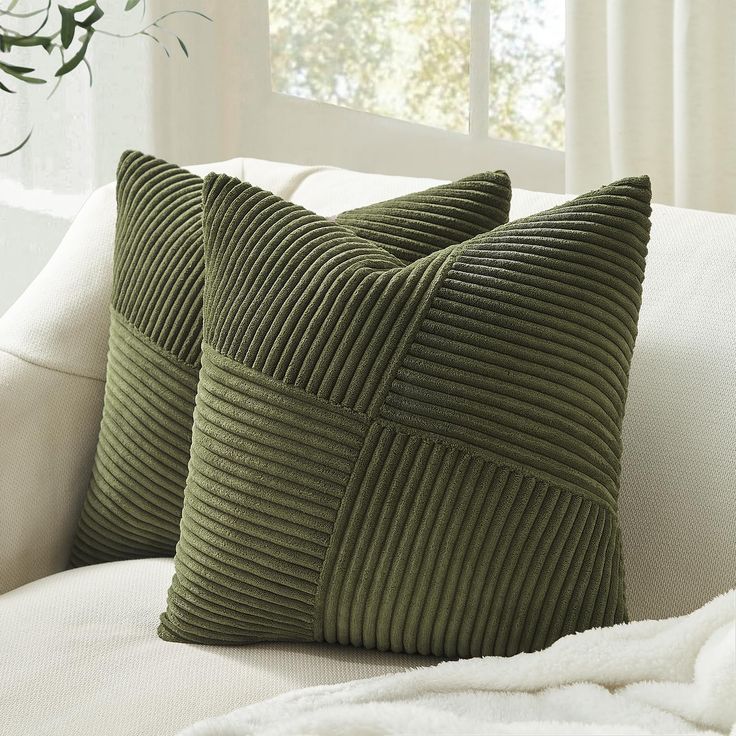 two green pillows sitting on top of a white couch next to a potted plant