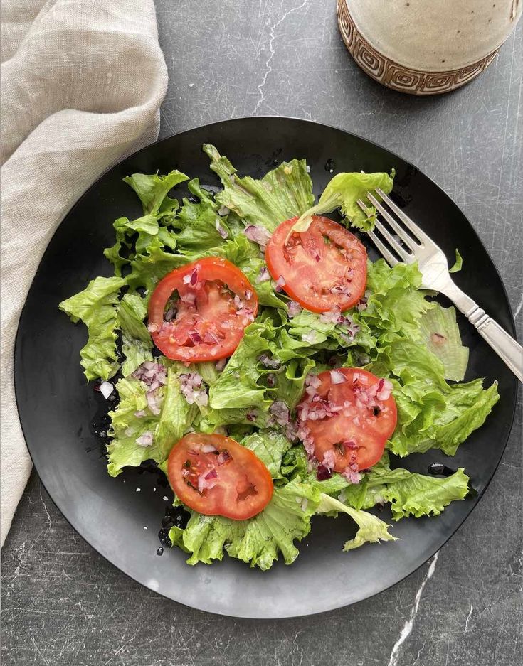 a black plate topped with lettuce and tomatoes