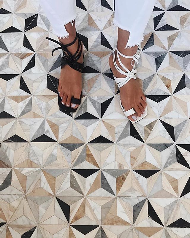 a woman standing on top of a tiled floor next to white pants and black sandals