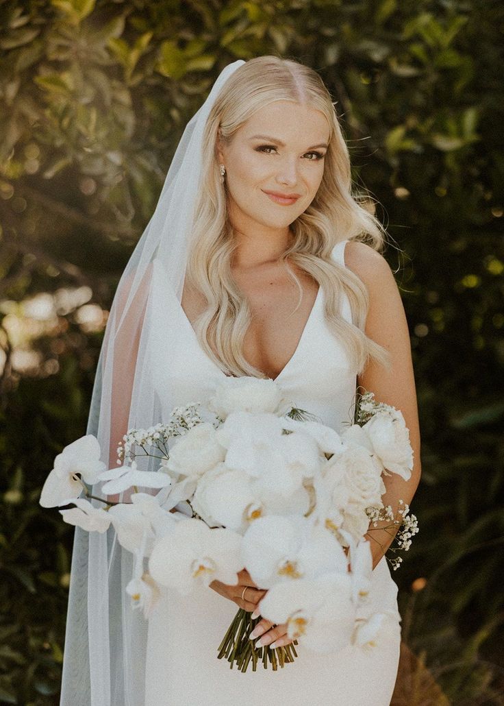 a woman in a wedding dress holding a bouquet of flowers and posing for the camera