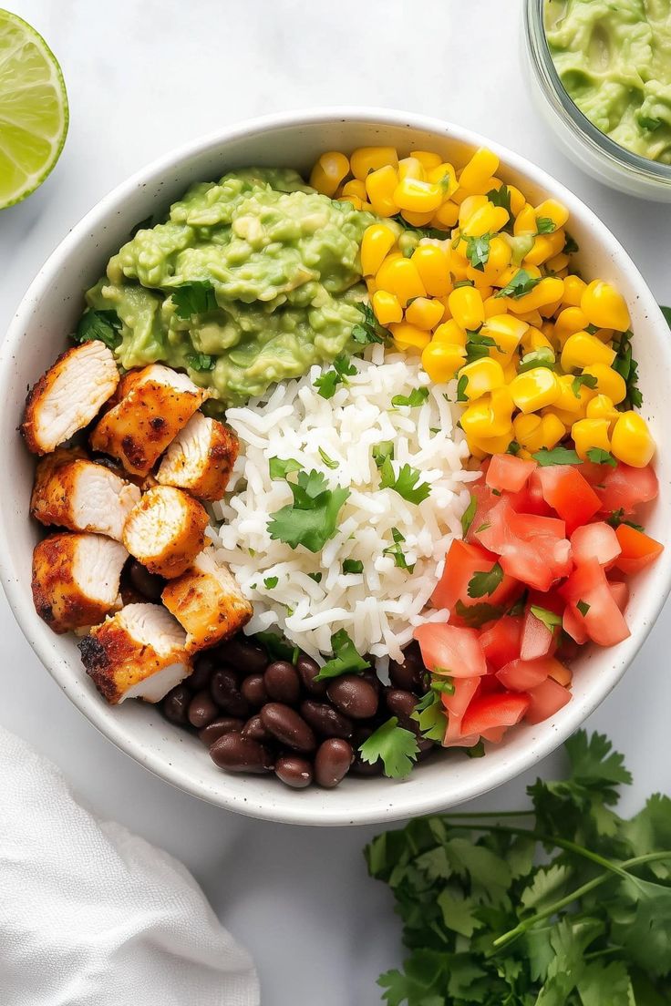 a bowl filled with chicken, rice, beans and avocado next to cilantro