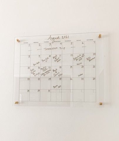 a glass calendar hanging on the wall with magnets and writing written on it's side