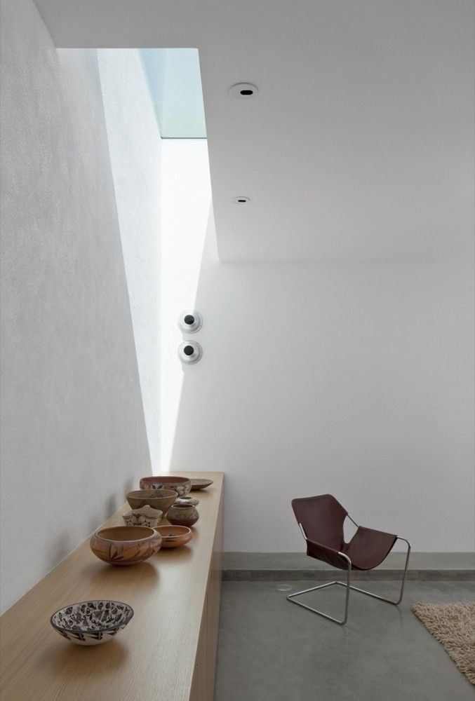 a chair and some bowls on a wooden table in a room with white walls that has a skylight above it