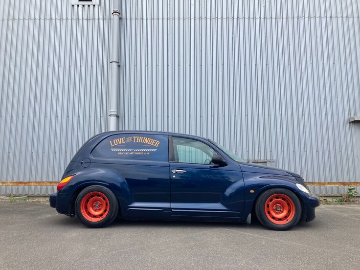 a blue car with orange rims parked in front of a metal building on the street