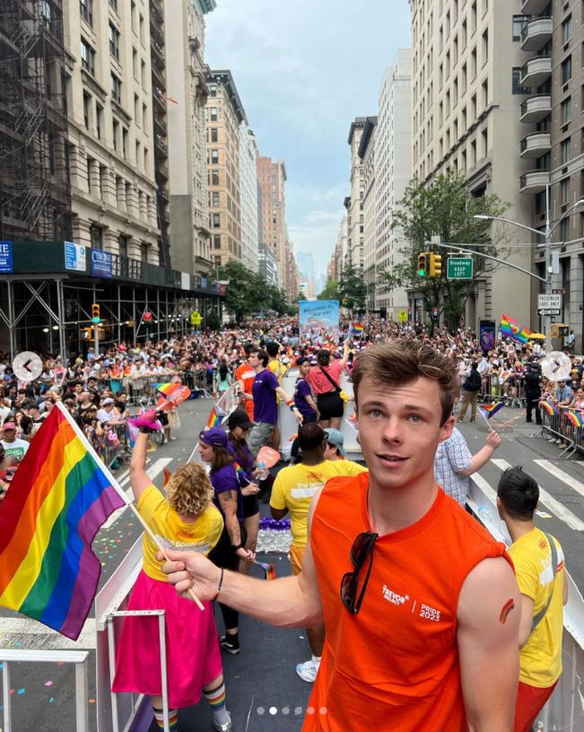 a man in an orange shirt is holding a rainbow flag and some people are walking down the street