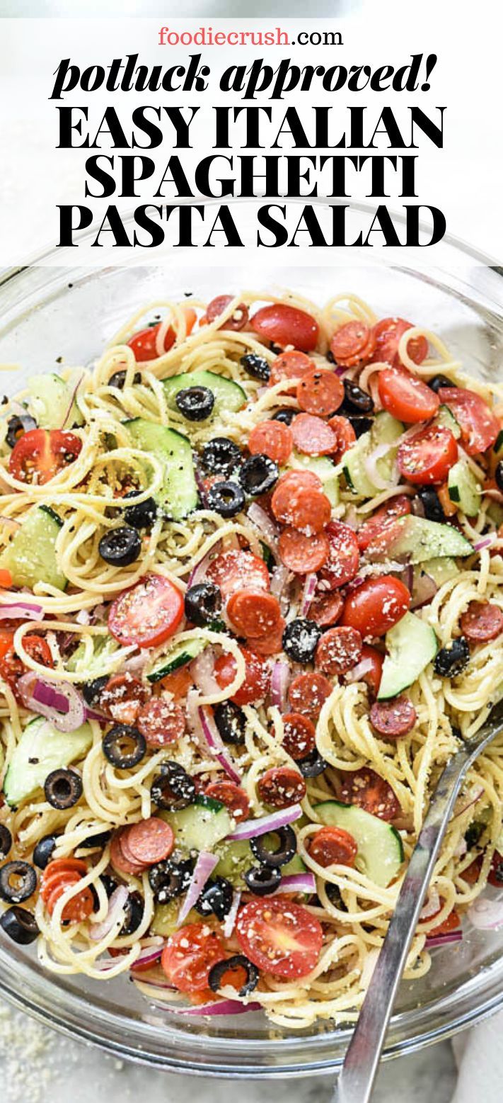 pasta with tomatoes, olives and other vegetables in a glass bowl next to a fork