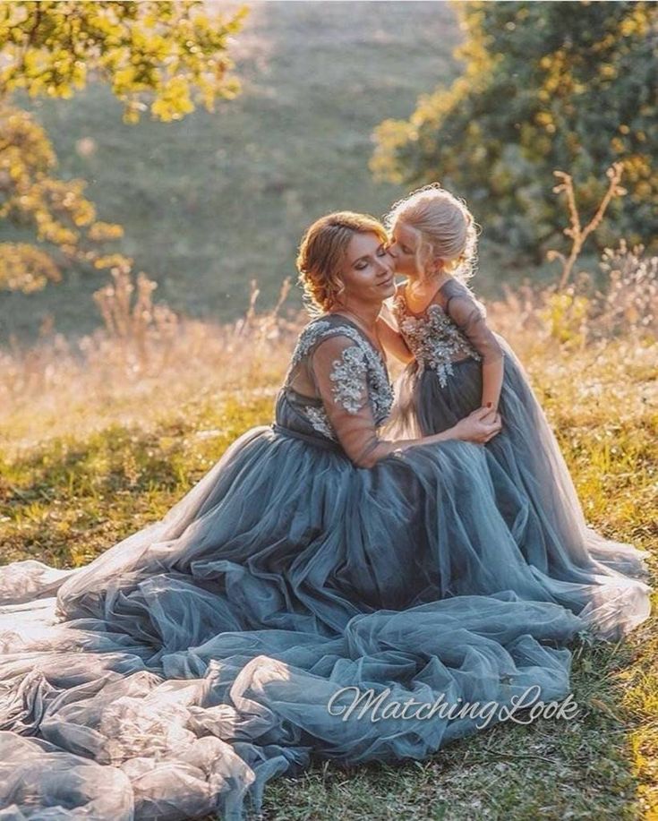 two women in dresses sitting on the ground with their arms around each other and smiling