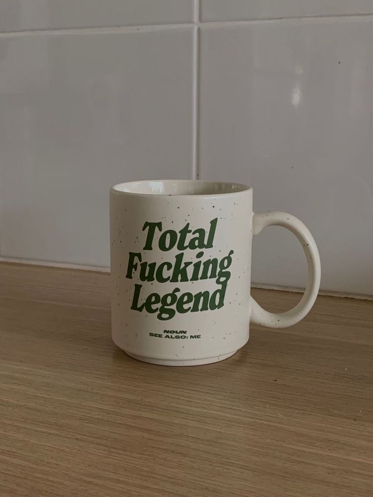 a white coffee mug sitting on top of a wooden table next to a tiled wall