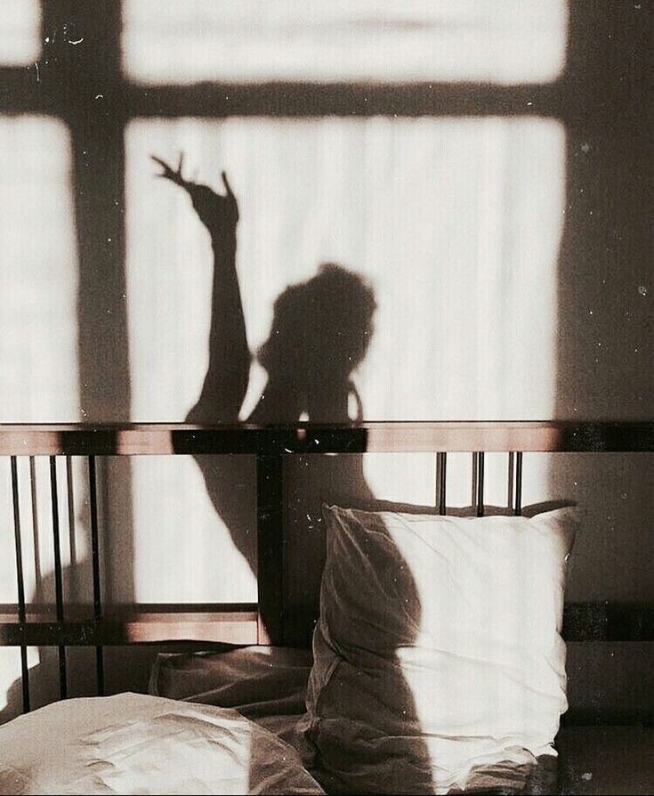 the shadow of a person standing on a bed in front of a window with white sheets