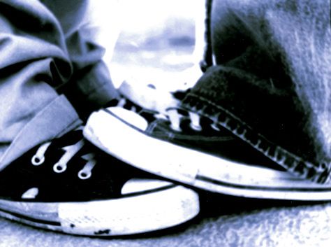 black and white photograph of two people's feet wearing converse shoes with one person standing on the ground