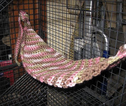 a crocheted pink and white blanket sitting in a cage next to a metal object