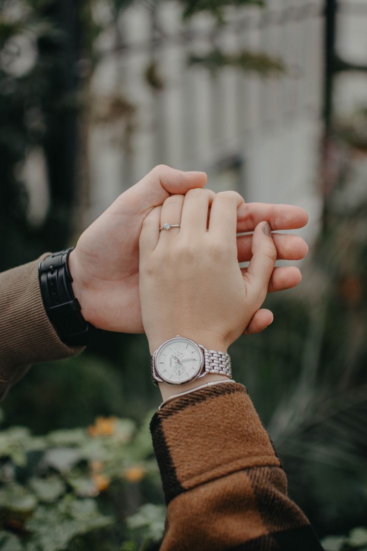 two people holding hands while standing next to each other in front of some plants and trees