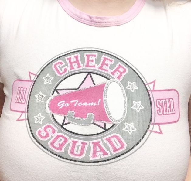 a woman wearing a cheer squad shirt with a pink bullhorn on it's chest