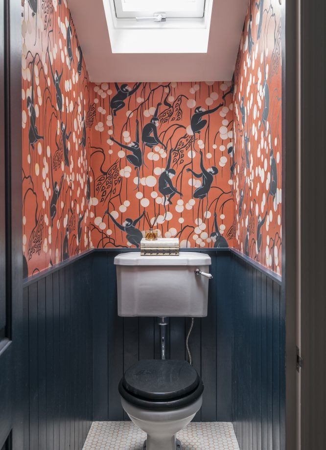 a small bathroom with an orange and blue wallpaper, white toilet and skylight