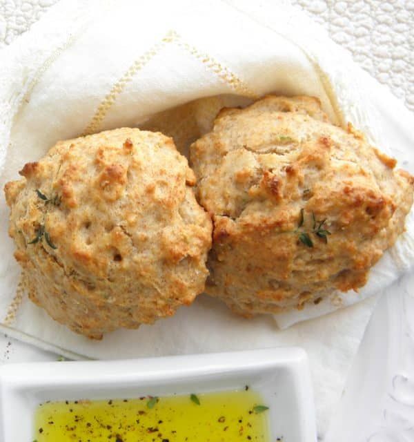 two muffins sitting on top of a white plate next to a bowl of oil