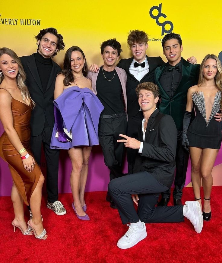 a group of people standing on top of a red carpet next to each other in front of a yellow and purple wall