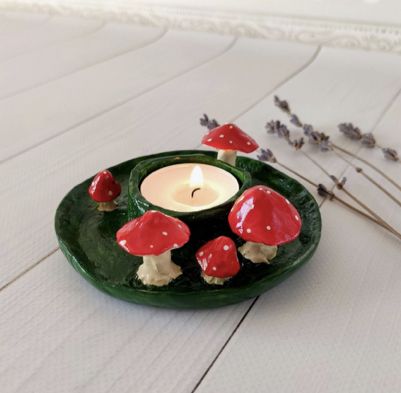 a candle that is sitting on top of a green plate with red mushrooms around it