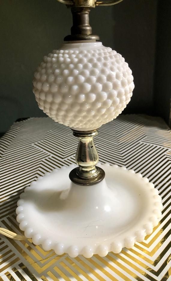 a white lamp sitting on top of a table next to a metal light shade holder