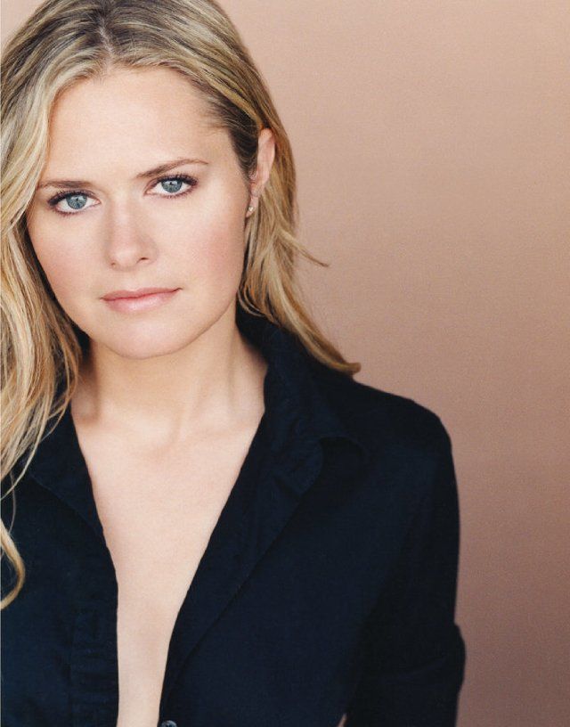 a woman with blonde hair and blue eyes wearing a black blazer posing for the camera