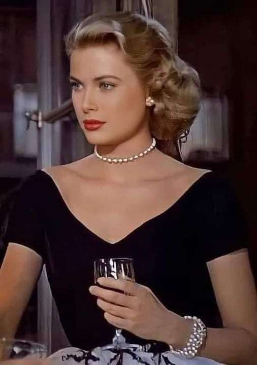 a woman in a black dress holding a wine glass and wearing a pearl choker