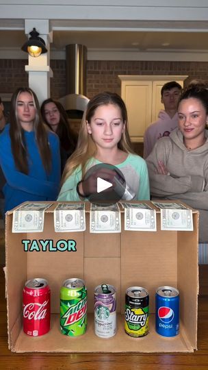 a group of people standing around a cardboard box filled with sodas and dollar bills