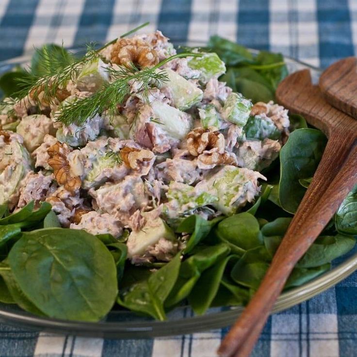 a salad with lettuce, chicken and walnuts on a plate next to a wooden spoon