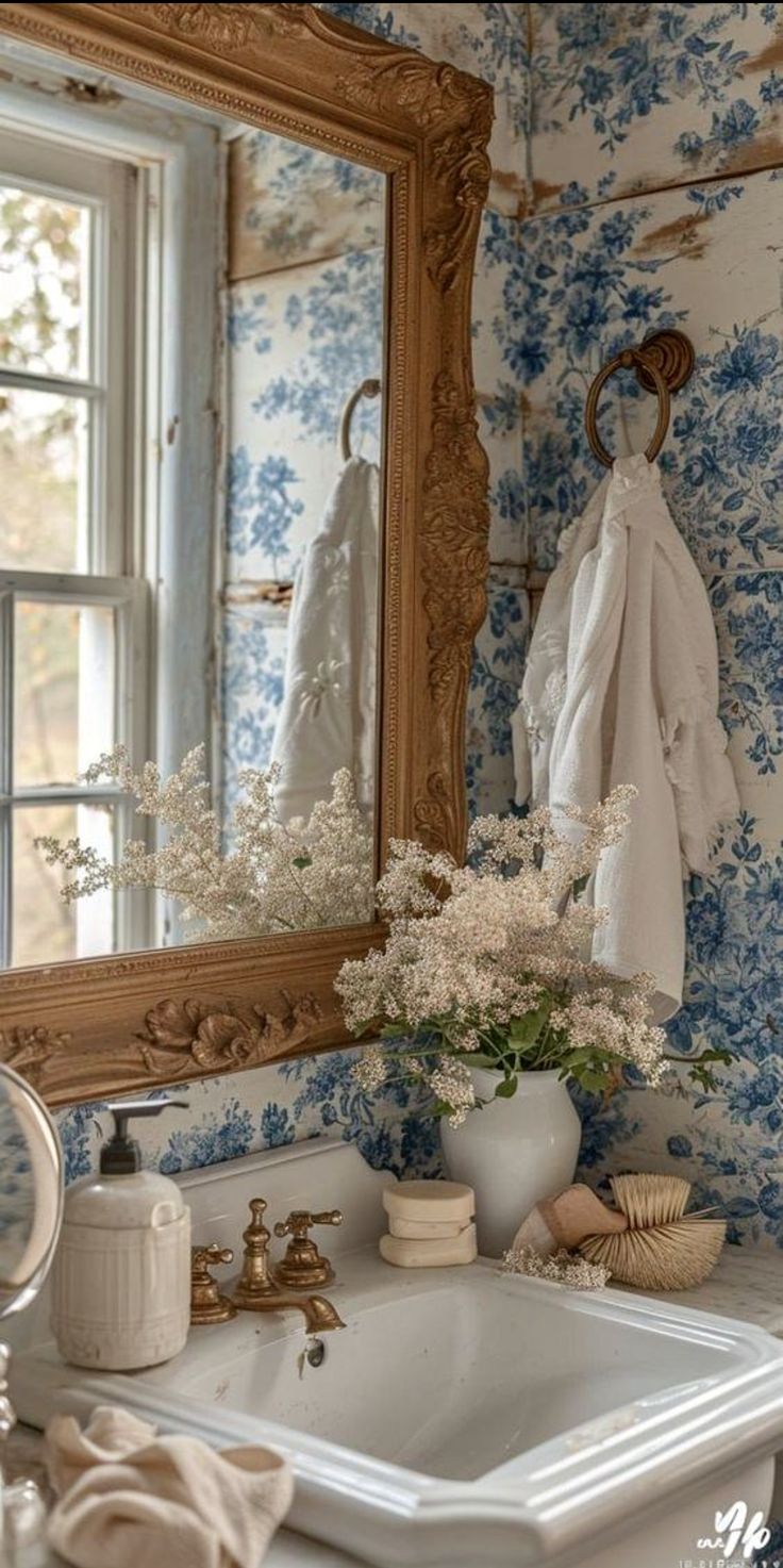 a bathroom sink sitting under a mirror next to a white vase with flowers in it