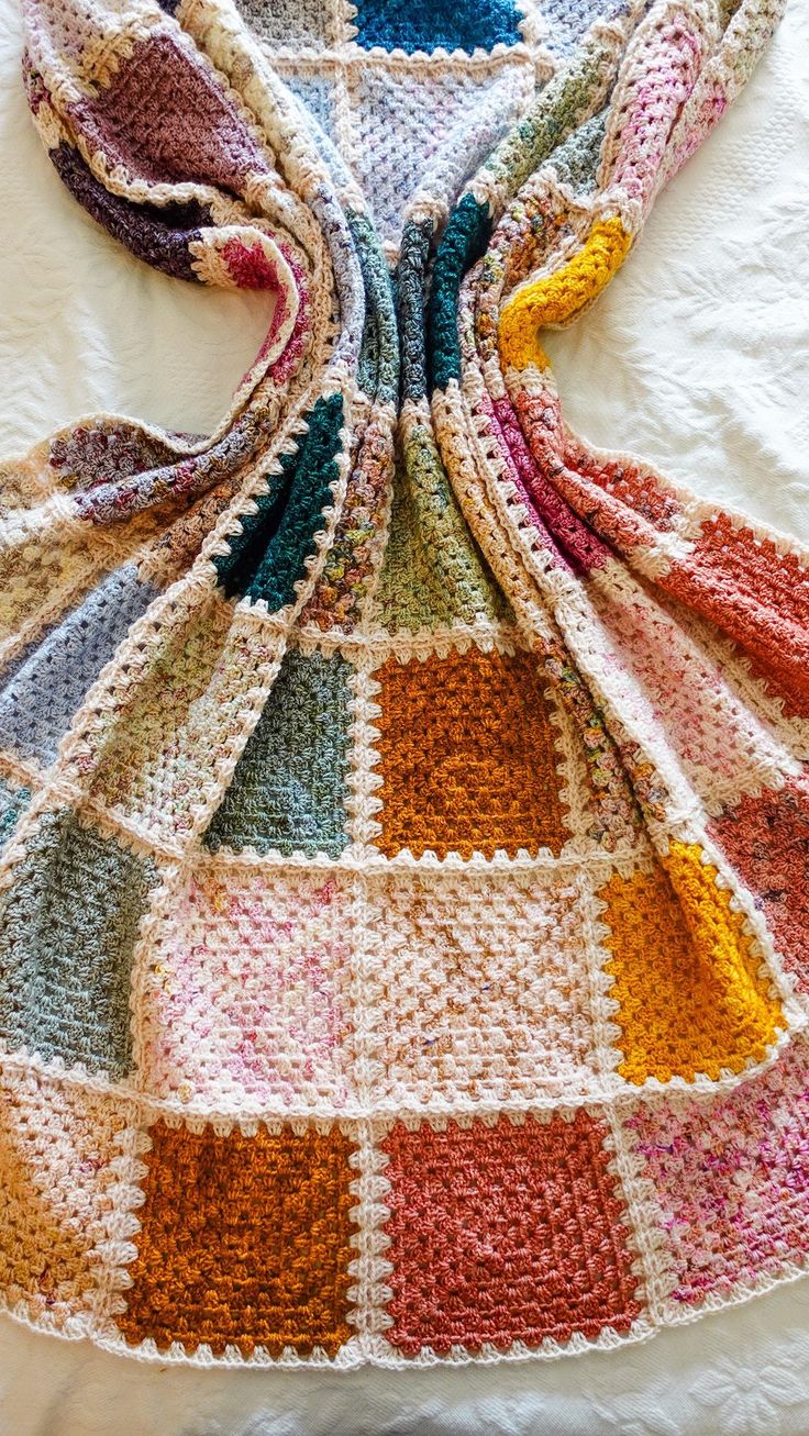 a multicolored crocheted blanket laying on top of a white bed sheet