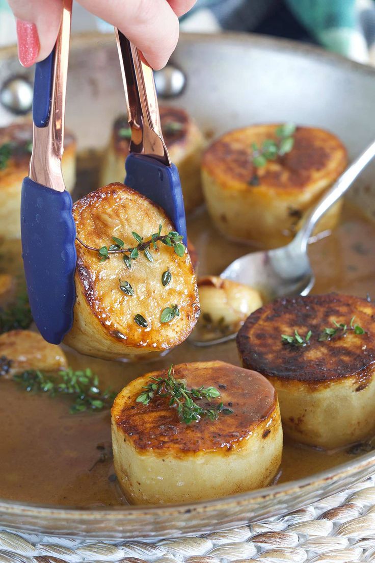 a person is holding tongs over some food in a pan with sauce and herbs