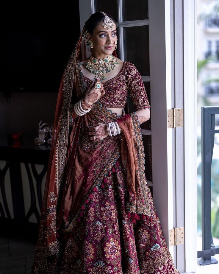 a woman in a red and gold bridal gown standing by a door with her hands on her hips