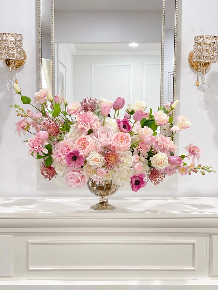 a vase filled with pink and white flowers sitting on top of a table next to a mirror