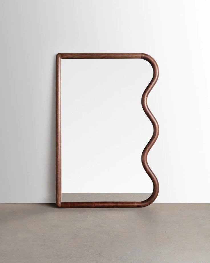 a mirror sitting on top of a cement floor next to a white wall with a wooden frame