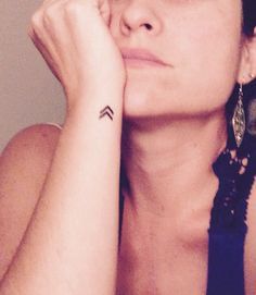 a woman is holding her hand to her face and has a small tattoo on her left arm