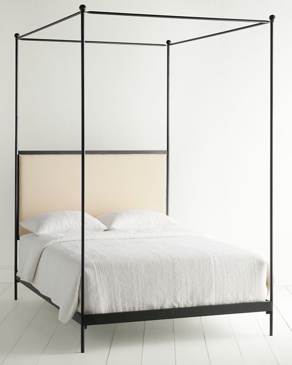 a four poster bed with white linens and black metal frame, in a minimalist bedroom