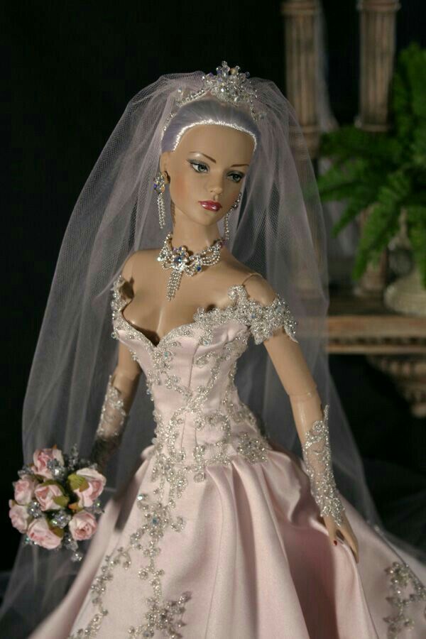 a barbie doll wearing a wedding dress and veil with flowers in her hand on a table