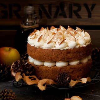 a cake with white frosting and pine cones on a black plate next to an apple