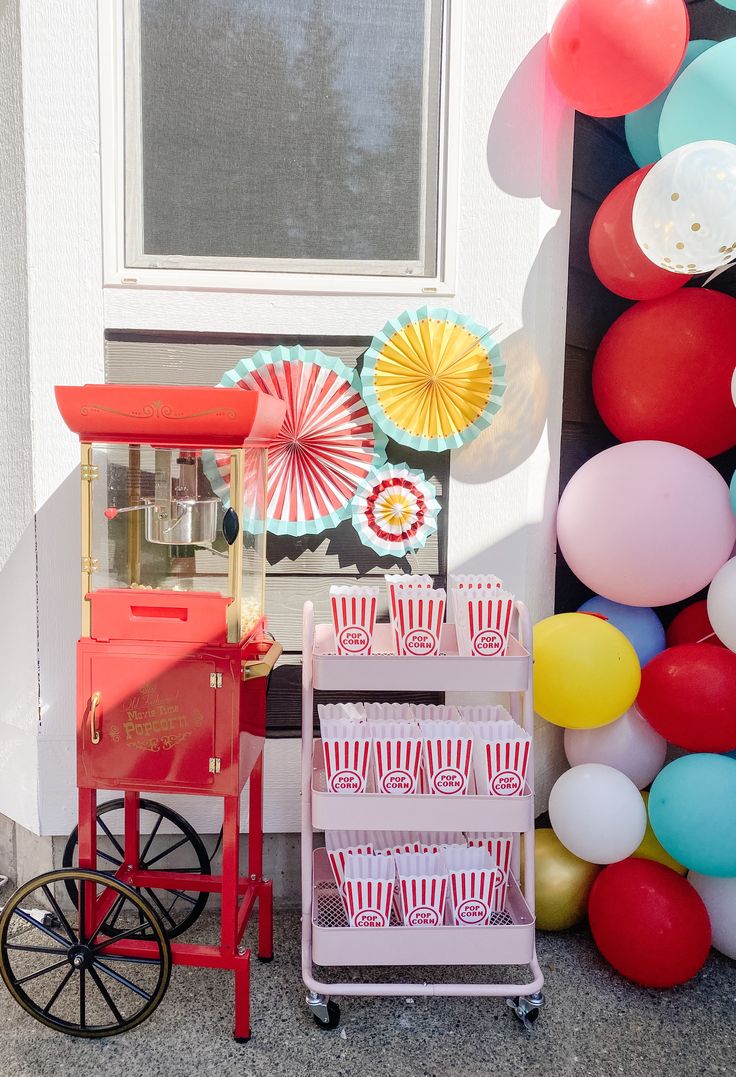 a red cart with popcorn on it next to balloons