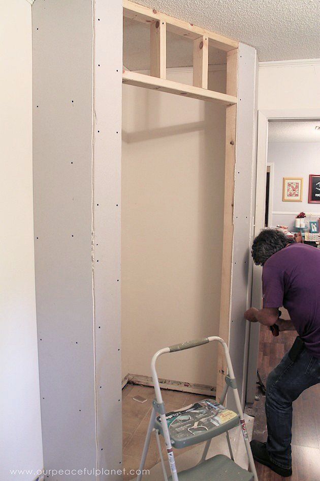 a man standing next to a ladder in front of a wall with unfinished shelves on it