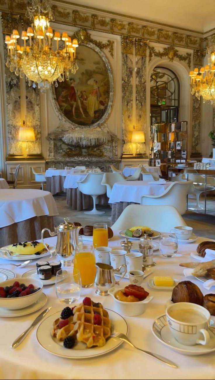 a table set for breakfast in a fancy room with chandeliers and white linens