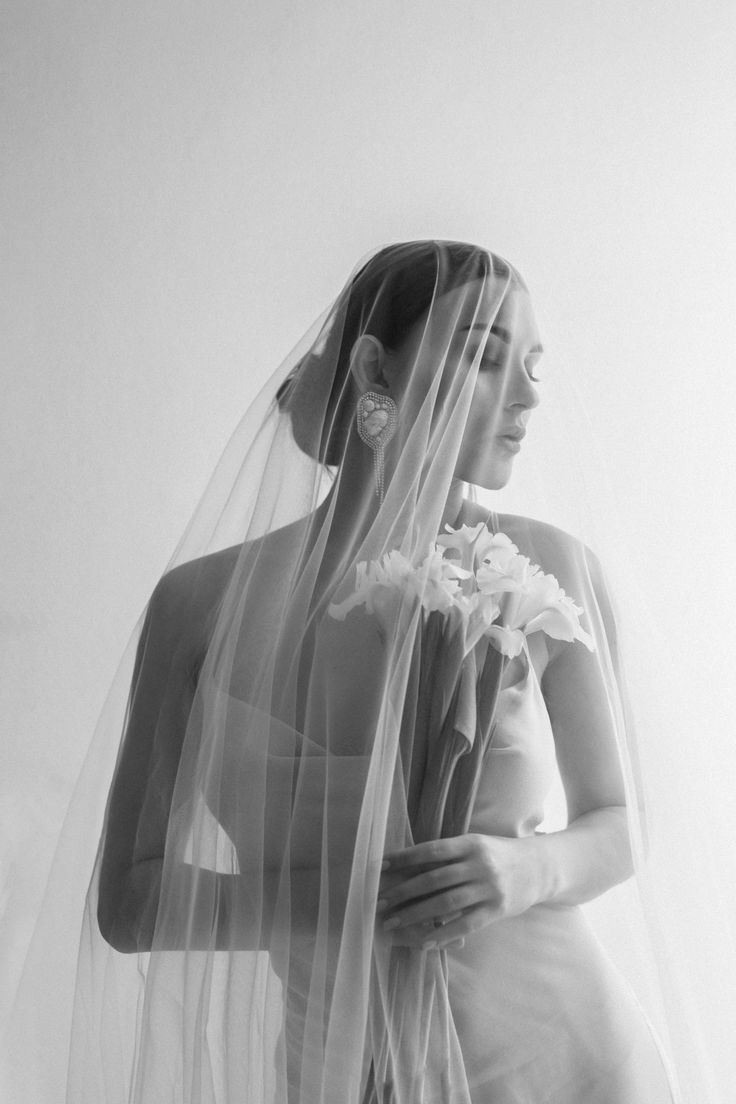 black and white photograph of a woman in wedding dress with veil over her head holding flowers