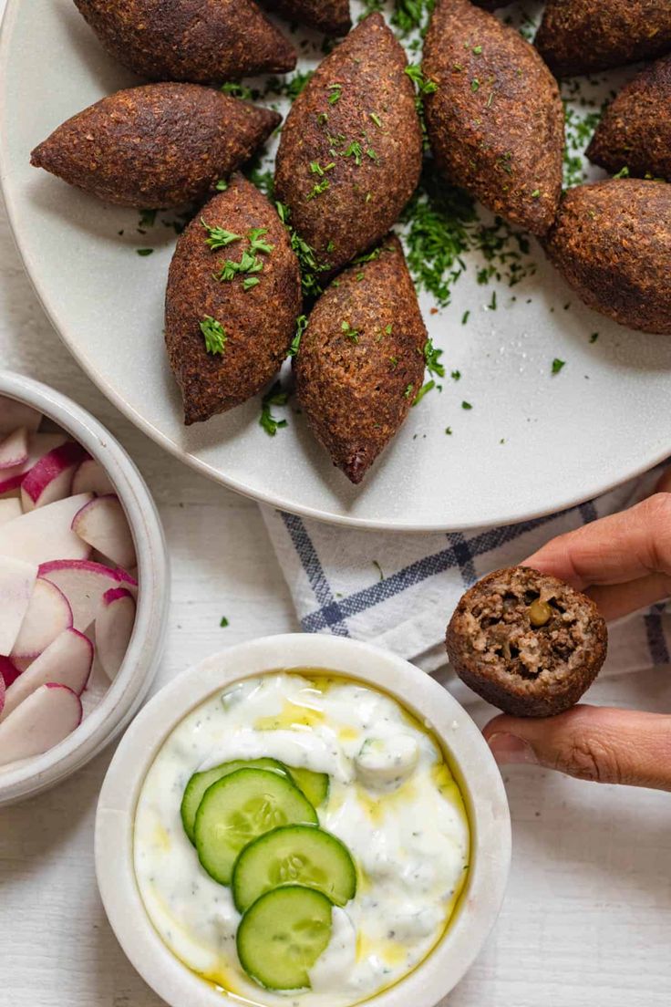 a white plate topped with cucumber and other food items next to a bowl of dip