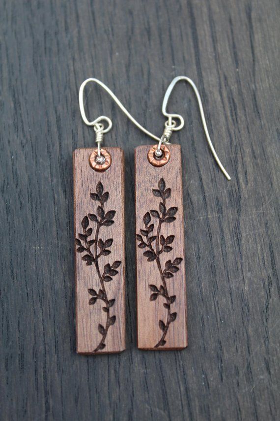 two wooden earrings with flowers on them sitting on top of a black table next to a pair of silver ear wires