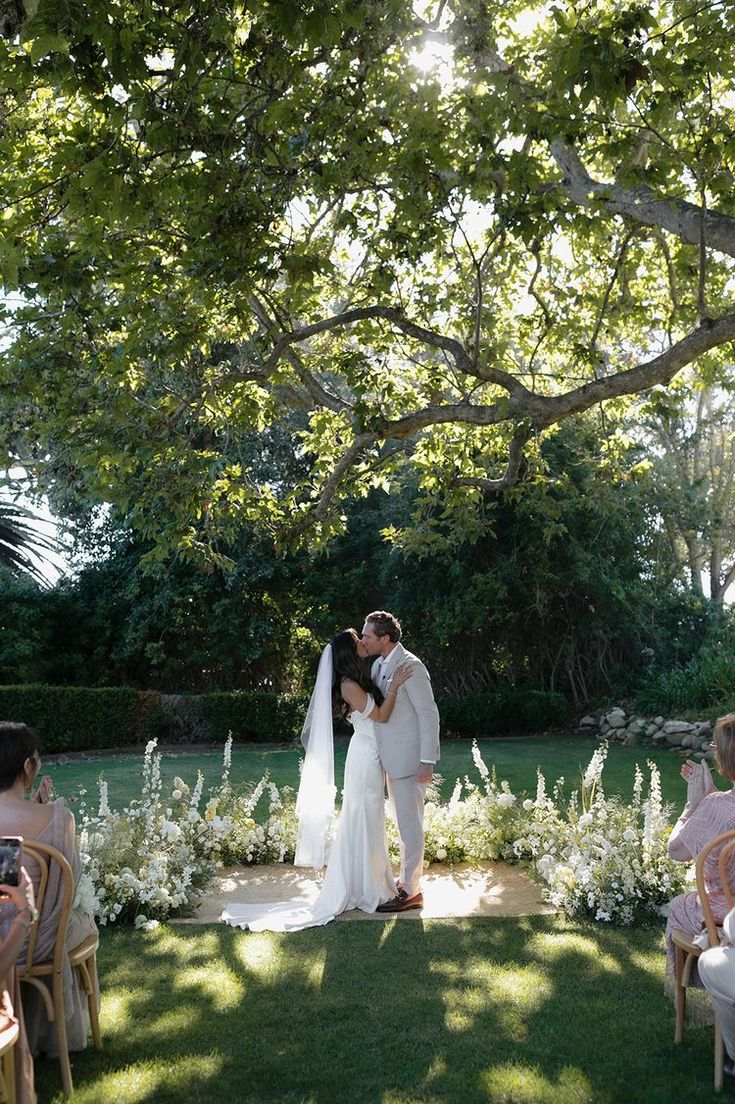 a bride and groom kiss in front of an outdoor ceremony